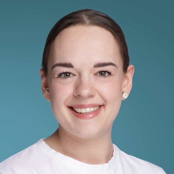 Sarah Eberhardt Porträt einer lächelnden Frau mit mittellangen Haaren vor einfarbigem Hintergrund.