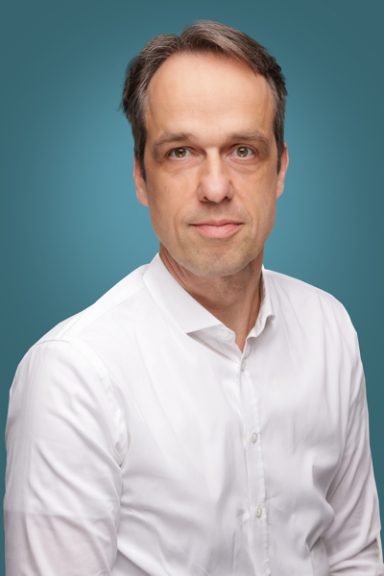 Prof. Dr. H. Nückel Mann mit kurzen Haaren in weißem Hemd vor einem einfarbigen Hintergrund.