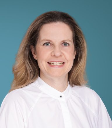 Dr. K. Nückel Porträt einer lächelnden Frau mit blonden Haaren vor einem blauen Hintergrund.